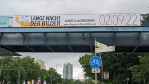 An einer Brücke in Berlin Lichtenberg hängt ein Brückenbanner. Auf der Brückenwerbung lädt Kunst in Lichtenberg zur Lange Nacht der Bilder ein.