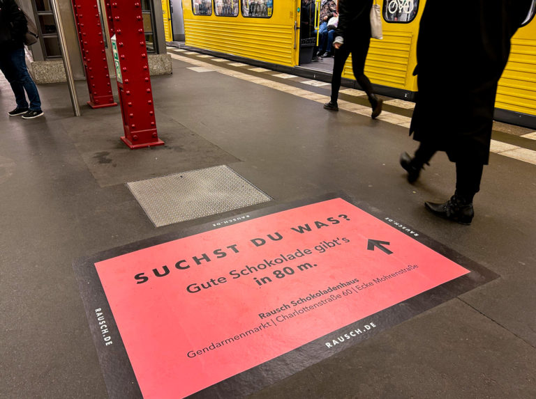 Pinke Bodenfolie mit Wegbeschreibung, klebt auf dem Boden eines Berliner-U-Bahnsteigs.
