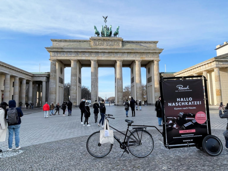 Vor dem Brandenburger Tor macht Schokoladen-Rausch eine Promotion und verteilt Süßigkeiten. An einem Rad ist ein Werbeanhänger befestigt.