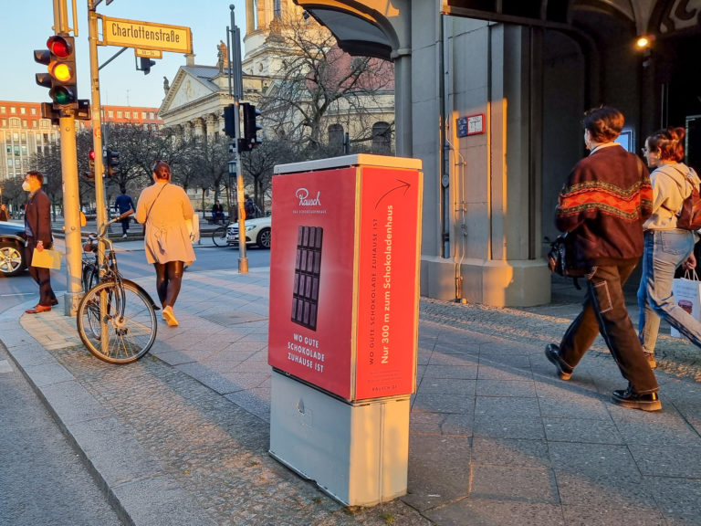 Stromkastenwerbung auf einer Straße in Berlin Mitte. Passanten laufen an der Außenwerbung vorbei.