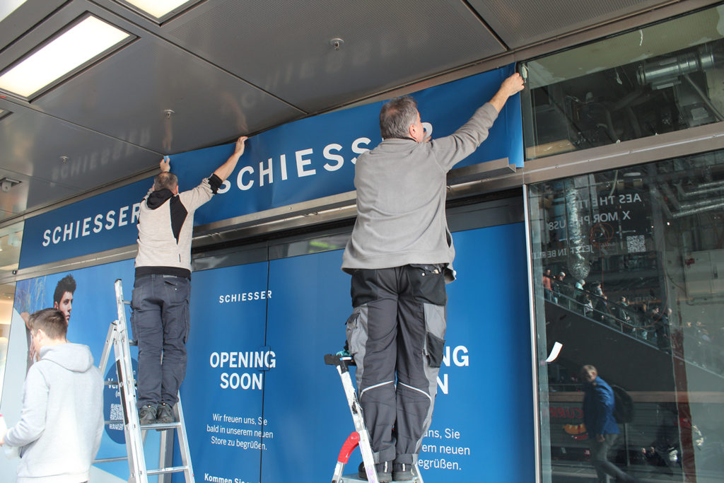 zwei Mitarbeiter bringen Schaufensterwerbung an