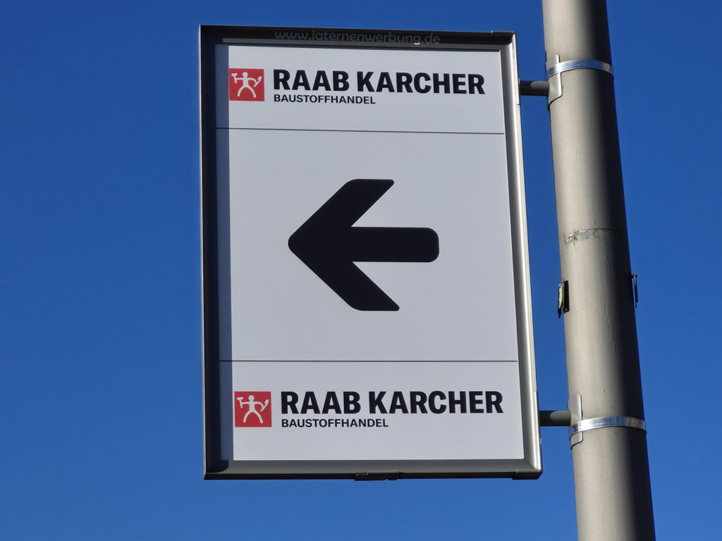 Schild an einem Laternenmast mit Werbung von Raab Karcher.