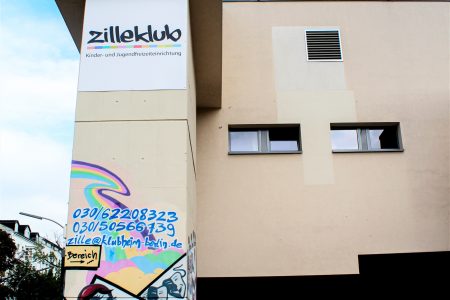 Ein großes Firmenschild für "Zille Klub" in Berlin welches an einer großen Häuserwand hängt. Ein Teil der Häuserfassade ist mit Graffiti besprüht.